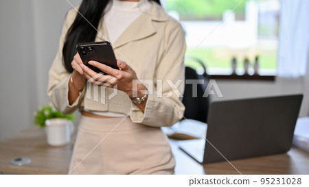 Cropped, Asian businesswoman standing in her office, using smartphone Cropped, Asian businesswoman standing in her office, using smartphone 95231028