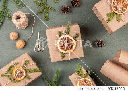 Boxes, craft paper, twine, scissors, dried oranges and natural decor for wrapping XMAS, New Year gifts on green background. Concept Zero waste Merry Christmas. Top view Flat lay Boxes, craft paper, twine, scissors, dried oranges and natural decor for wrapping XMAS, New Year gifts on green background. Concept Zero waste Merry Christmas. Top view Flat lay 95232023