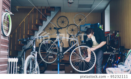 Experienced mechanic in casual clothes is busy checking handlebar and front wheel of bicycle then adjusting and fixing it with tools. Repairing cycles and people concept. 95232111