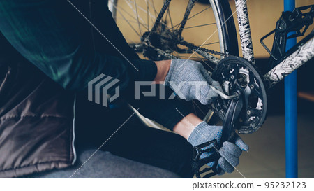 Close-up shot of strong male hands in protective gloves repairing broken bicycle treadle tightening loose joint with allen wrench in nice cozy workplace. 95232123