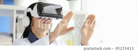 Young female doctor in virtual reality headset works on computer in hospital office Young female doctor in virtual reality headset works on computer in hospital office 95233413