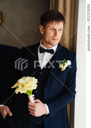 the groom is in a dark blue suit with a boutonniere and a bouquet of callas. the groom is in a dark blue suit with a boutonniere and a bouquet of callas. 95233856