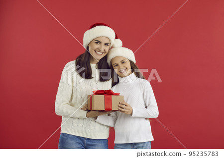 Happy young mom and teen daughter holding christmas present while standing on red background. 95235783