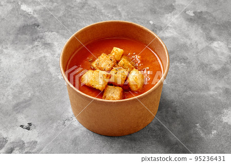 Cold gazpacho soup with toasts, dried herbs in paper bowl on gray stone surface Cold gazpacho soup with toasts, dried herbs in paper bowl on gray stone surface 95236431
