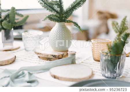 Ceramic and glass vases with Christmas tree branches on wooden stands for a festive family dinner Ceramic and glass vases with Christmas tree branches on wooden stands for a festive family dinner 95236723