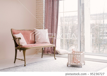 A pink vintage sofa with pillows stands near the window in the living room or children's room in the house. Minimalistic interior design 95236727