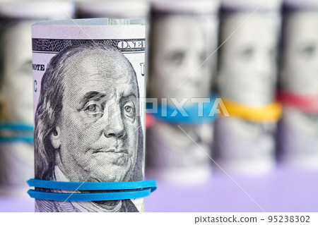 Rolled hundred dollar bills with rubber band on the background of dollar bills Rolled hundred dollar bills with rubber band on the background of dollar bills 95238302