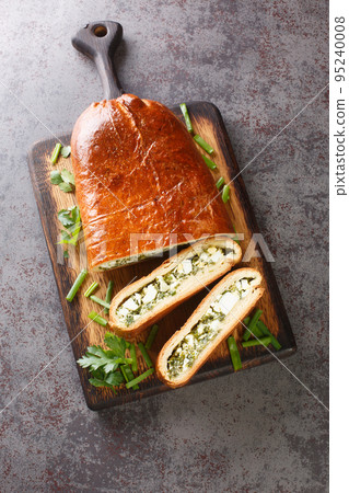 Delicious savory pie stuffed with boiled eggs, green onions, parsley, dill and spinach close-up on a wooden board. Vertical top view 95240008