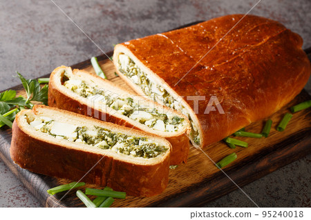 Homemade delicious pie stuffed with boiled eggs, green onions, parsley, dill and spinach close-up on a wooden board. Horizontal 95240018