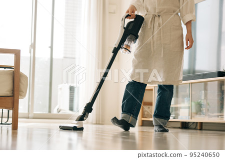 Woman vacuuming in the living room 95240650