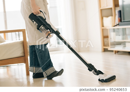 Woman vacuuming in the living room 95240653