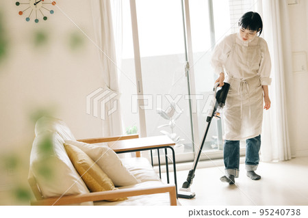 Woman vacuuming in the living room 95240738
