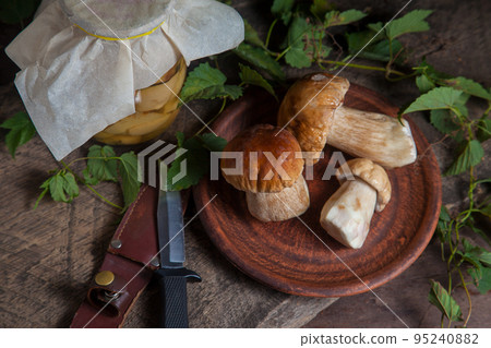 Clay plate with porcini mushroom commonly known as Boletus Edulis, glass jar with canned mushrooms and knife on vintage wooden background.. Clay plate with porcini mushroom commonly known as Boletus Edulis, glass jar with canned mushrooms and knife on vintage wooden background.. 95240882