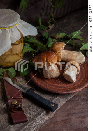 Clay plate with porcini mushroom commonly known as Boletus Edulis, glass jar with canned mushrooms and knife on vintage wooden background.. 95240883