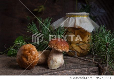 Two porcini mushrooms commonly known as Boletus Edulis and glass jar with canned mushrooms on vintage wooden background.. Two porcini mushrooms commonly known as Boletus Edulis and glass jar with canned mushrooms on vintage wooden background.. 95240884