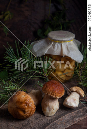 Three porcini mushrooms commonly known as Boletus Edulis and glass jar with canned mushrooms on vintage wooden background.. Three porcini mushrooms commonly known as Boletus Edulis and glass jar with canned mushrooms on vintage wooden background.. 95240886