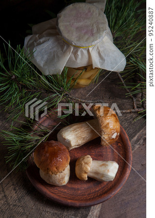 Clay plate with three porcini mushrooms commonly known as Boletus Edulis and glass jar with canned mushrooms on vintage wooden background.. 95240887