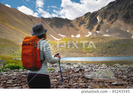 woman with a backpack walks near the mountains and a blue lake. Travel and hobby concept Back view 95243545