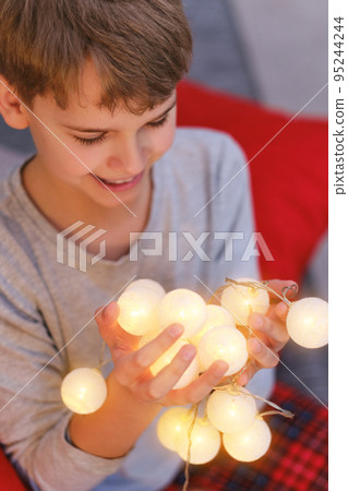 Close-Up Of Teenage Boy With Illuminated Christmas Lights At Home Close-Up Of Teenage Boy With Illuminated Christmas Lights At Home 95244244