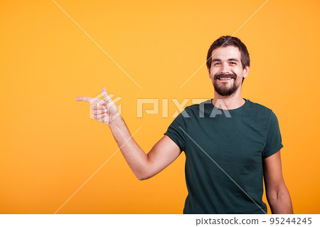 Cheerful smiling man pointing at his right at copyspace available for your advertisement or promotion. Isolated on orange backgorund in studio. Cheerful smiling man pointing at his right at copyspace available for your advertisement or promotion. Isolated on orange backgorund in studio. 95244245