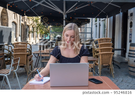 Attractive young blonde business woman using her laptop while sitting outdoors in a European city at Attractive young blonde business woman using her laptop while sitting outdoors in a European city at 95246816