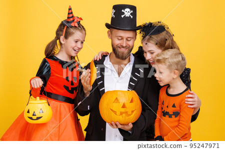 Cheerful family in carnival costumes celebrate Halloween with jack-o-lantern on colored yellow background Cheerful family in carnival costumes celebrate Halloween with jack-o-lantern on colored yellow background 95247971