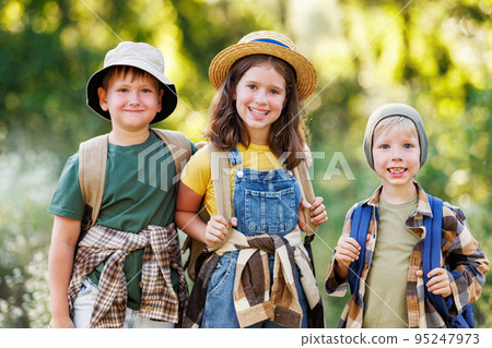 Cheerful children tourists with backpacks went hiking on a summer day and smiles at the camera 95247973