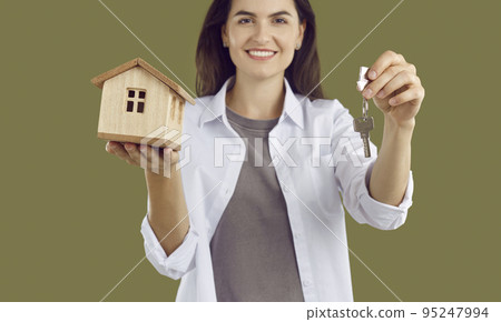 Woman in a white shirt is holding a wooden mock-up of a house and the keys to the house. Woman in a white shirt is holding a wooden mock-up of a house and the keys to the house. 95247994
