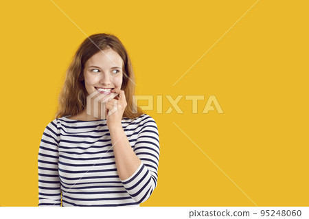 Woman with funny awkward smile on face looks sideways on yellow copy space background 95248060
