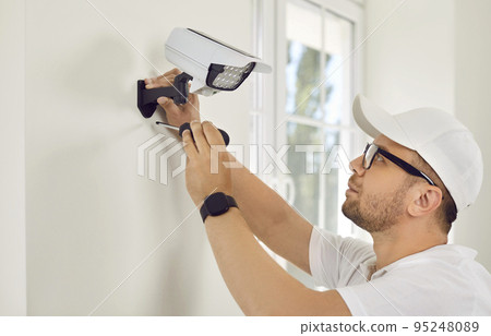Worker installs security camera with LED light on wall. Worker installs security camera with LED light on wall. 95248089