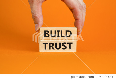 Build trust symbol. Concept words Build trust on wooden blocks on a beautiful orange table orange background. Businessman hand. Business and build trust concept, copy space. Build trust symbol. Concept words Build trust on wooden blocks on a beautiful orange table orange background. Businessman hand. Business and build trust concept, copy space. 95248323