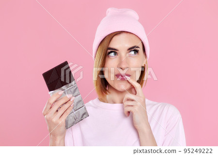 blonde woman in t-shirt and hat holding chocolate bar 95249222