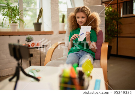 Cute little elementary schoolgirl studying online, looking video lesson on smartphone. Kids at-home activity, creativity and distant education 95249385
