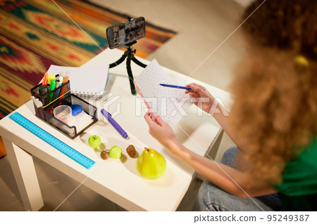 Cute little elementary schoolgirl studying online, looking video lesson on smartphone. Kids at-home activity, creativity and distant education 95249387