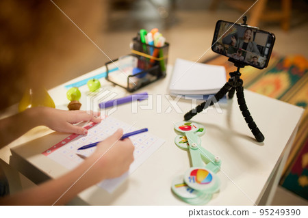 Cute little elementary schoolgirl studying online, looking video lesson on smartphone. Kids at-home activity, creativity and distant education 95249390