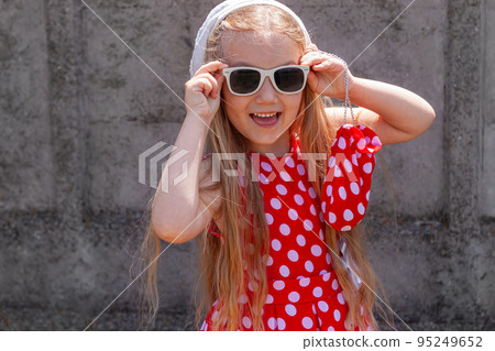 Beautiful happy girl in a red polka dot dress smiling on on concrete wall background. Cute joyful child with long hair. Beautiful happy girl in a red polka dot dress smiling on on concrete wall background. Cute joyful child with long hair. 95249652