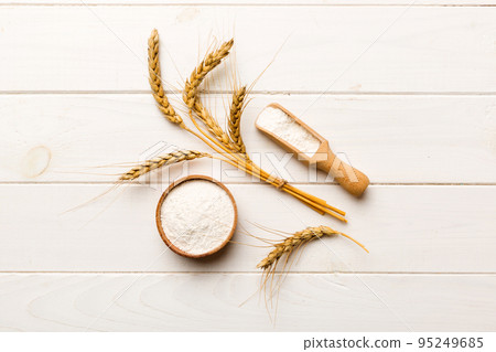 Flat lay of Wheat flour in wooden bowl with wheat spikelets on colored background. world wheat crisis Flat lay of Wheat flour in wooden bowl with wheat spikelets on colored background. world wheat crisis 95249685