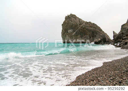 A large rock on a sea beach in the surf. Sea waves crash on the rocks A large rock on a sea beach in the surf. Sea waves crash on the rocks 95250292