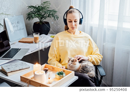 Relaxed young woman with cat sitting near table with burning candles and aroma sticks at home and do meditation and relaxation 95250408