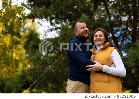 a happy husband joyfully hugs his wife against the backdrop of an autumn forest a happy husband joyfully hugs his wife against the backdrop of an autumn forest 95251309