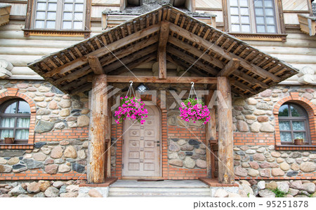 Wooden porch with massive shutters and hanging flowerpots under the roof in a stone building 95251878