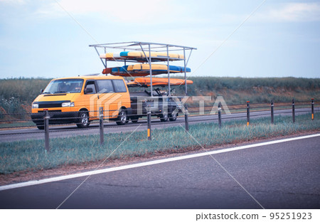An orange minibus transports a trailer with kayaks for swimming on the river. Travel and recreation. Copy space for text 95251923