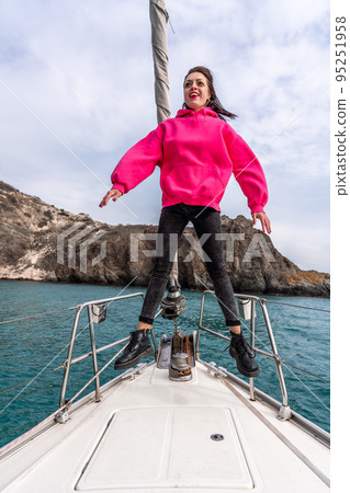 Woman standing on the nose of the yacht at a sunny summer day, breeze developing hair, beautiful sea on background 95251958