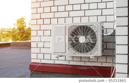 Wall-mounted industrial air conditioner on a brick wall of a building. Maintenance and repair of air conditioners. Sunset 95251983