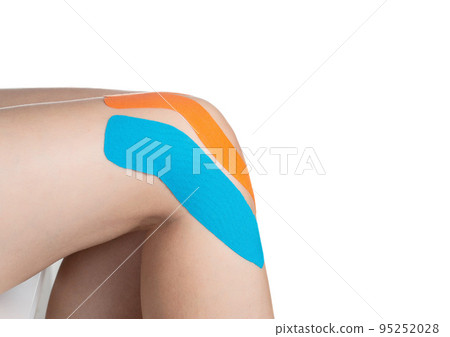 Female knee joint with orange and blue tape for microcirculation and joint fixation. White background, isolate, close-up 95252028