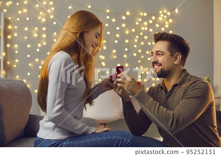 Happy young man proposing to his beloved woman and giving her gold engagement ring 95252131