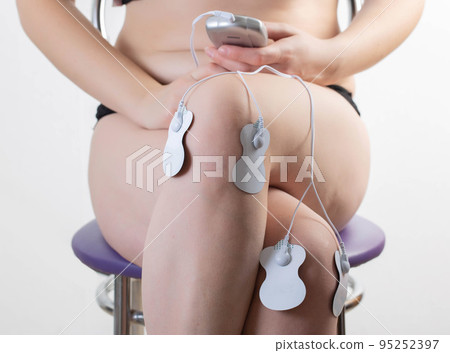 Electrodes of modern acupuncture and anti-cellulite massagers on the legs of a girl in problem areas. Home physiotherapy, close-up 95252397