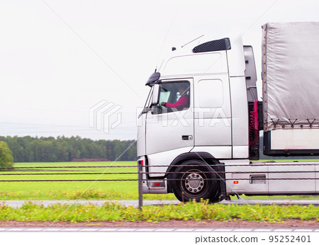 A truck driver drives a truck tractor in cloudy weather on a motorway in summer. Copy space for text. The mode of work and rest of truck drivers. 95252401