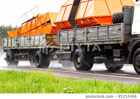 A truck with a semi-trailer transports oversized cargo on a wet road in rainy weather. 95252406