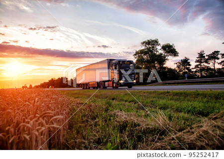 A black truck tractor transports cargo against the backdrop of a field and sunset in the evening. Profitable rate of road freight transport and freight turnover, statistics 95252417
